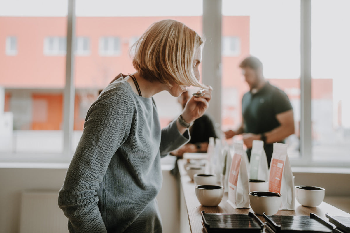 Frau probiert J. Hornig Spezialitätenkaffee aus einer Tasse mit einem Löffel, stellt "Cupping" dar. 