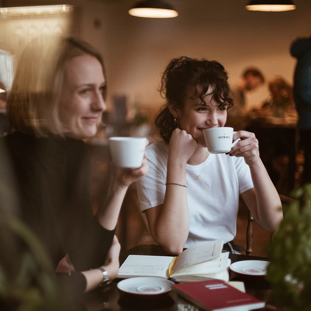 Zwei junge Frauen sitzen in einem Kaffeehaus und trinken einen Kaffee aus einer J. Hornig Tasse.