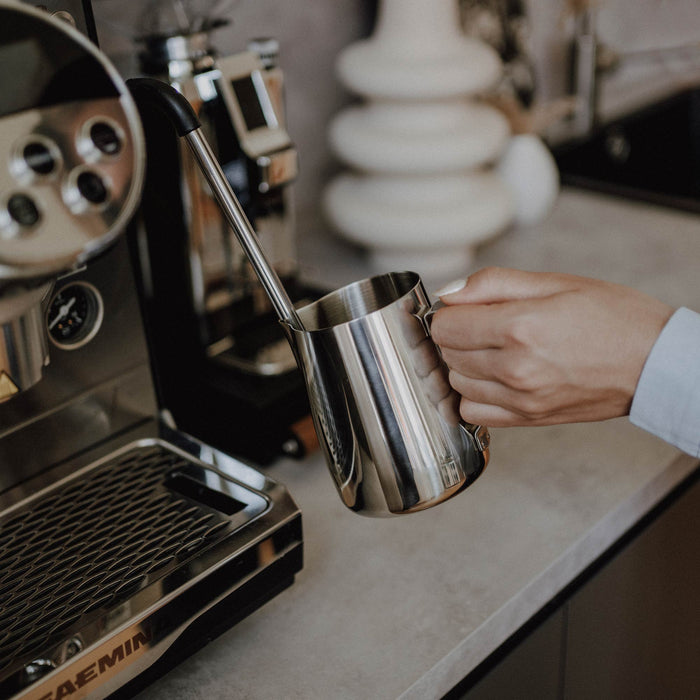 Eine Milchkanne aus Edelstahl mit einer Siebträgermaschine.